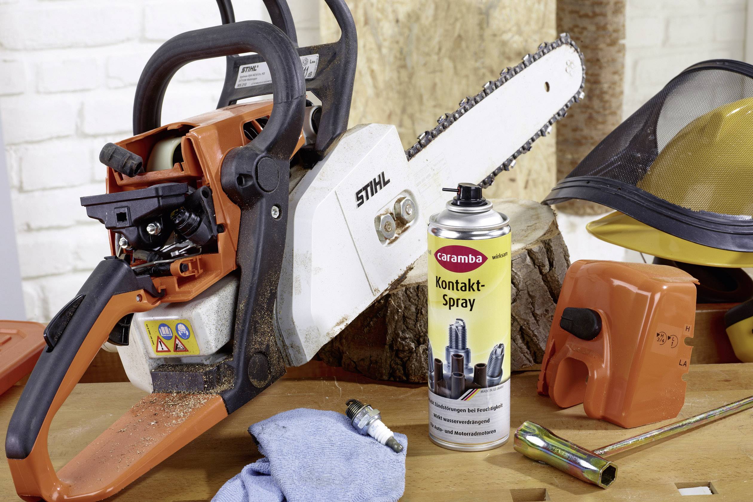 Tronçonneuse avec casque de protection, gants et spray de contact sur un établi.