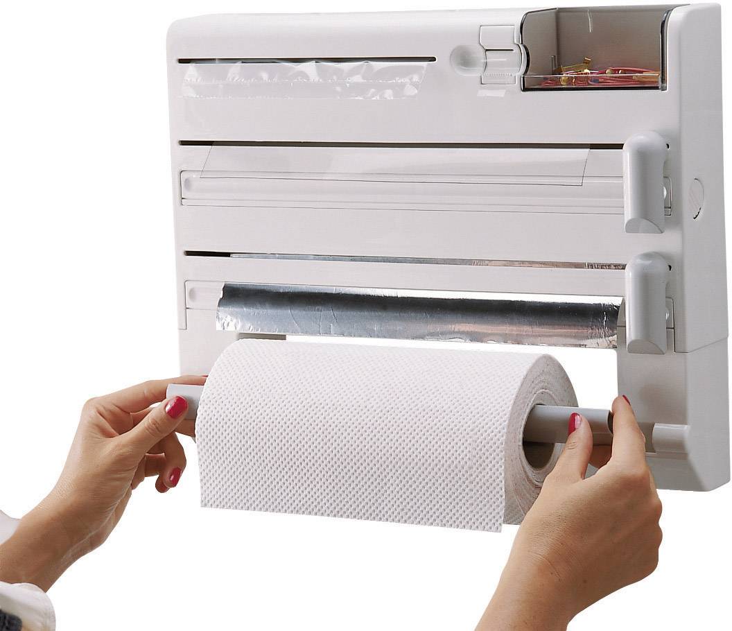 Une personne installe un rouleau de papier sur un support de papier essuie-tout avec un distributeur de film alimentaire et de film étirable fixé au mur.