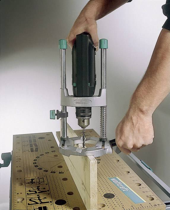 Une personne fore un trou dans une planche en bois à l'aide d'une perceuse à main sur un établi.