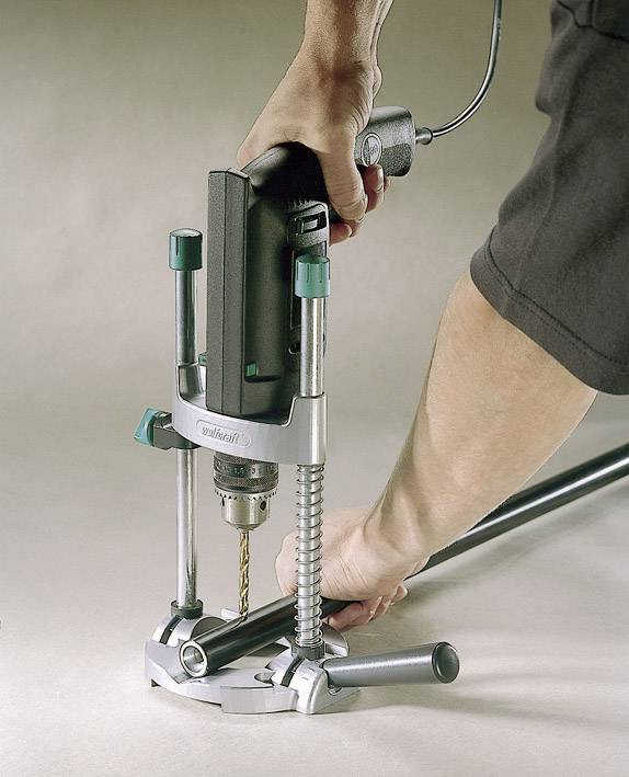 Une personne tient une perceuse qui est fixée dans un support de guidage et fore avec précision un trou dans un tube posé sur une table.