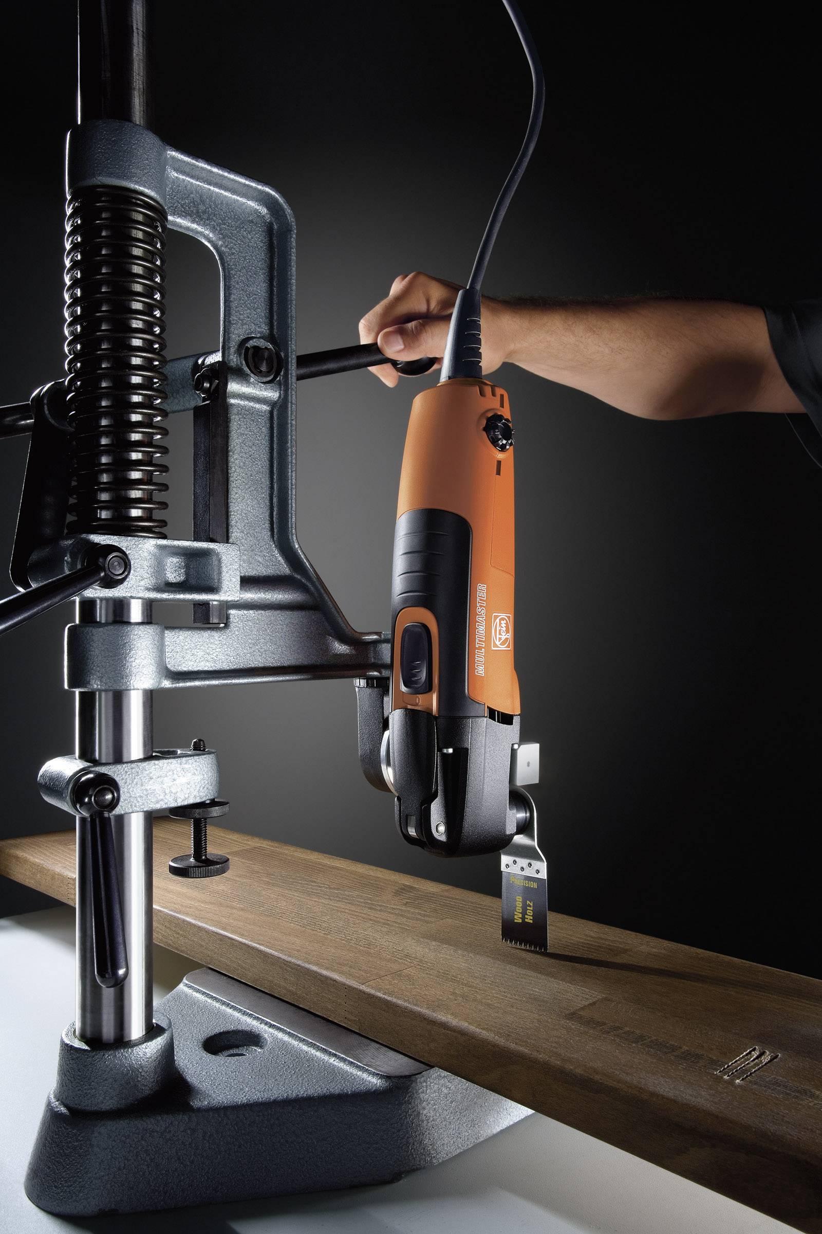Une scie électrique orange coupe du bois, montée sur un support de perceuse. Une main tient la scie pour assurer la précision.