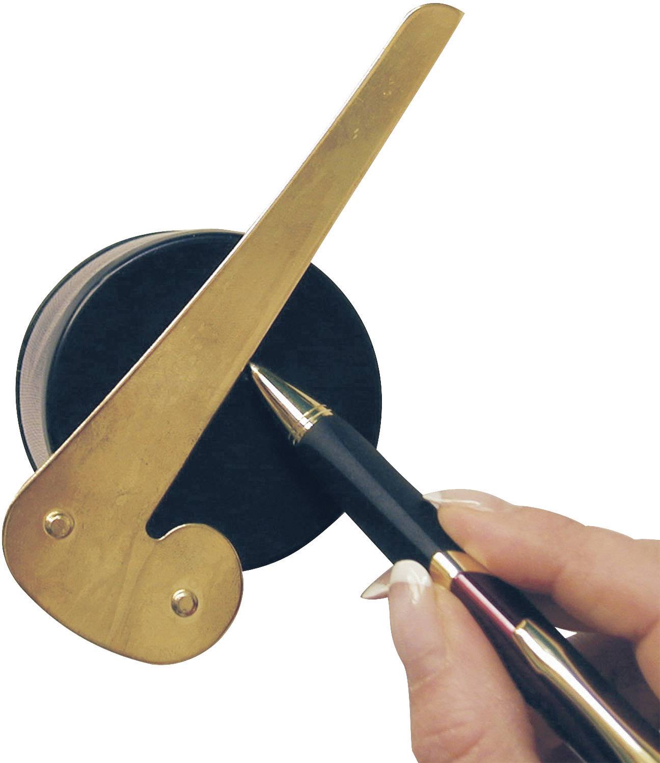 Une main tient un stylo-plume qui pointe vers un objet noir et rond avec un bras doré.