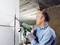 Un homme en tenue de protection utilise une scie électrique verte pour découper une entaille dans le Mur. Une situation de chantier est clairement identifiable.