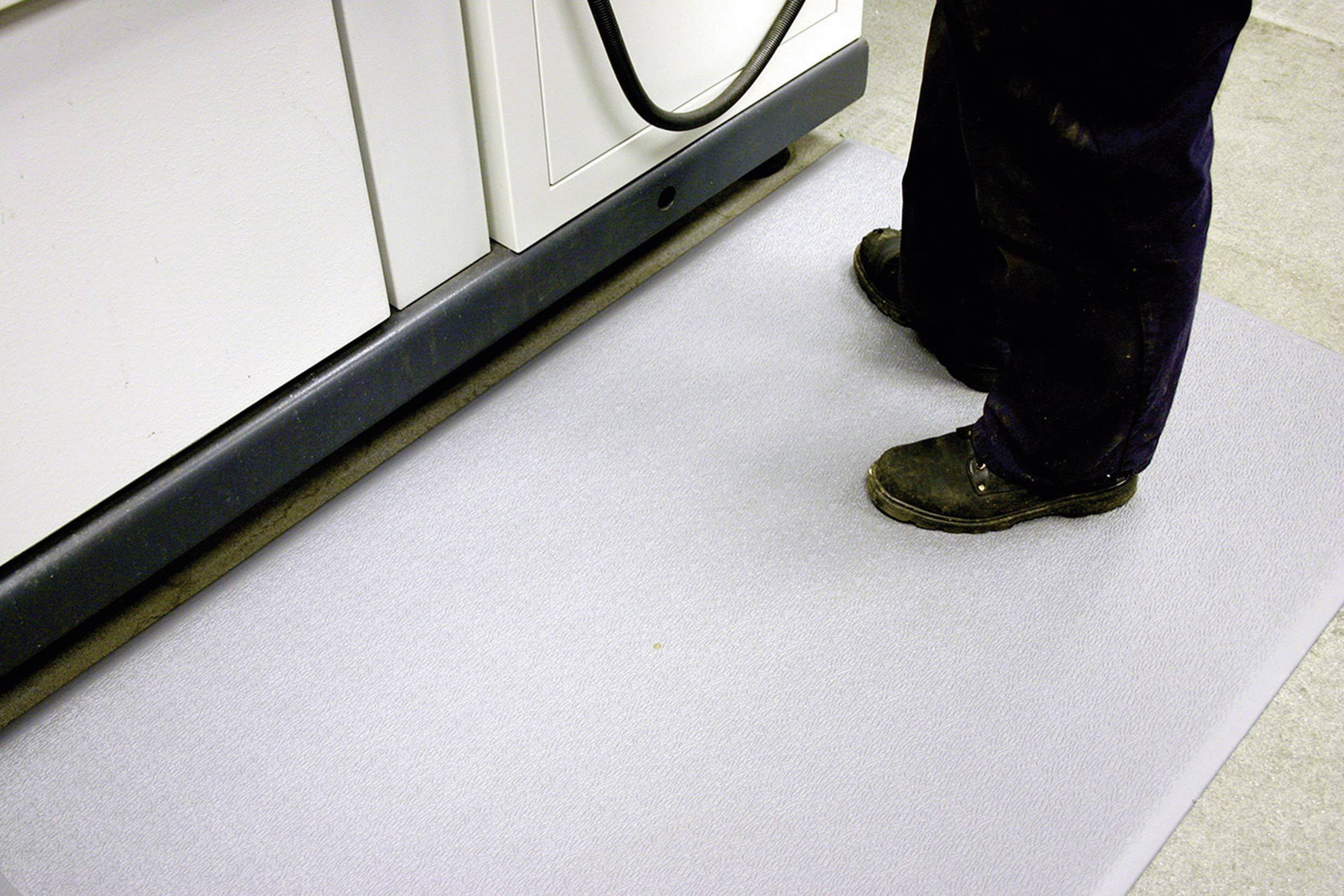 Une personne se tient sur un tapis ergonomique gris devant un meuble de cuisine blanc.