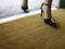 Une personne portant des talons hauts noirs franchit le seuil d'une porte sur un tapis marron. En arrière-plan, un sol pavé est visible.