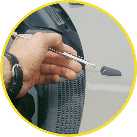 Une main tient un outil magnétique au-dessus de la carrosserie d'un véhicule pour redresser une petite bosse.