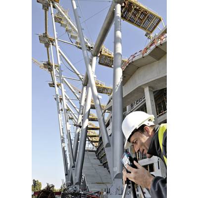 Un ouvrier portant un casque mesure à l'aide d'un appareil sur une construction en acier moderne sur un chantier de construction.