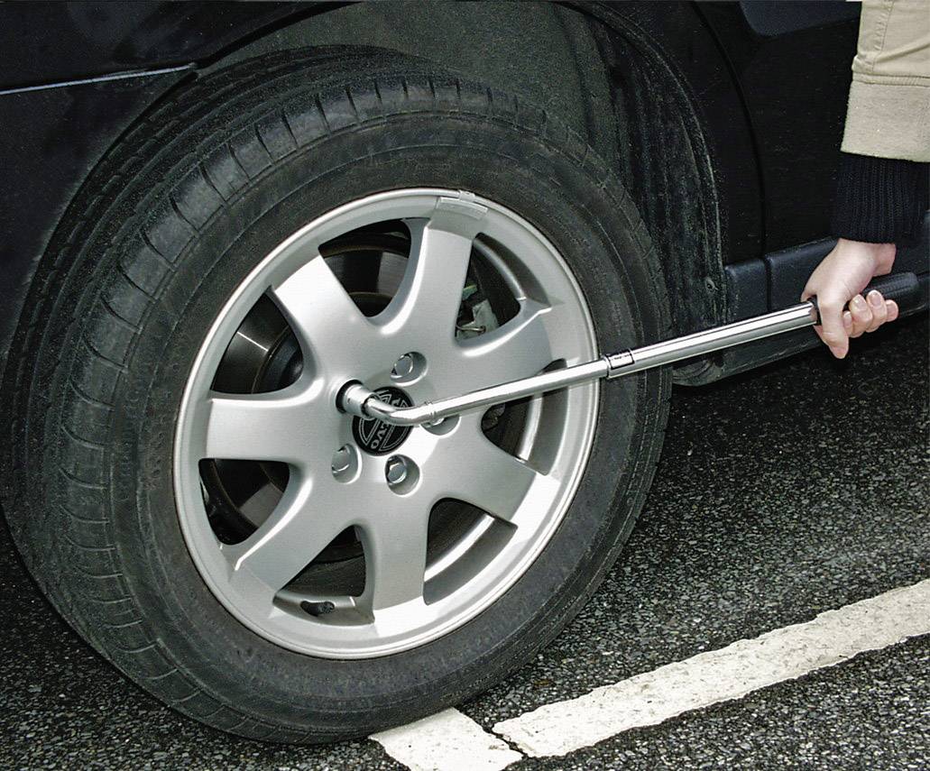 Une personne resserre les écrous de roue d'une voiture à l'aide d'une clé à molette. La voiture est garée sur un sol asphalté.