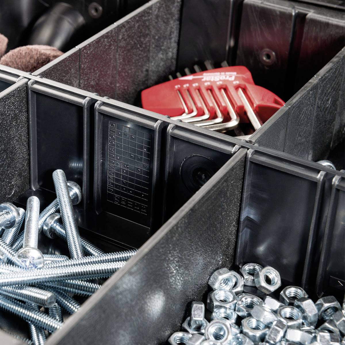 Une boîte à outils contenant des vis et des clés Allen dans plusieurs compartiments. Les vis sont en métal, les clés Allen sont rouges.