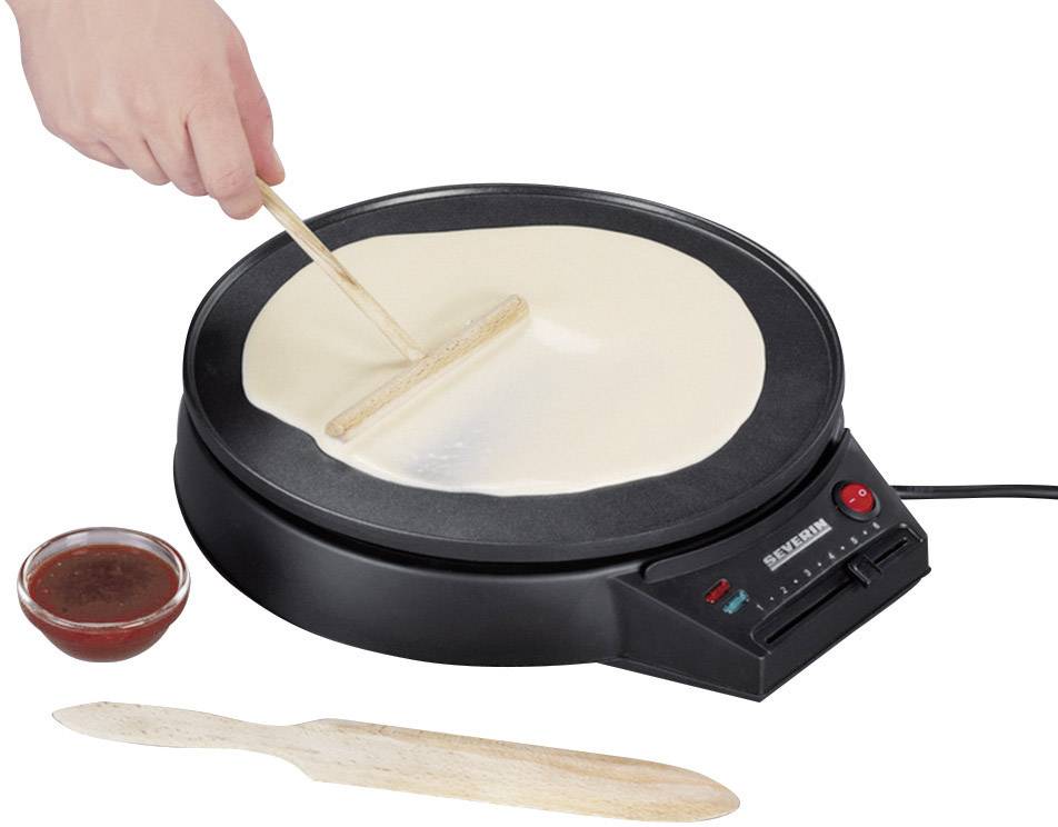 Une main étale de la pâte avec une spatule en bois sur une plaque crêpière électrique ronde. À côté, un bol de sauce.