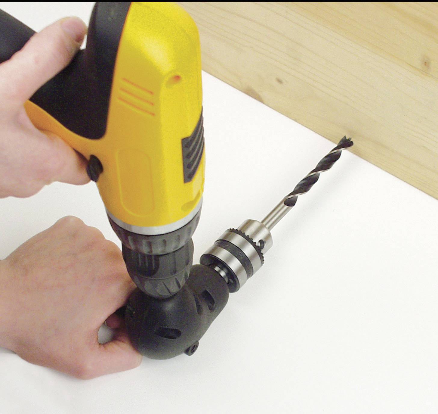 Une personne tient un dispositif noir dans sa main gauche, avec un tournevis-perceuse jaune équipé d'un foret inséré dedans.