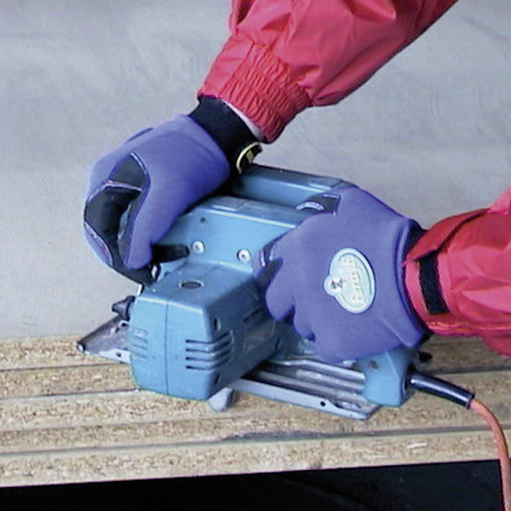 Une personne porte des gants de protection rouges et bleus et utilise une meuleuse bleue pour poncer les bords de panneaux de bois.