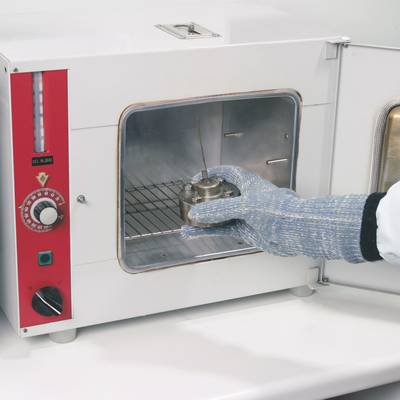 Une personne portant des gants place un échantillon de métal dans un étuve de laboratoire ouverte.