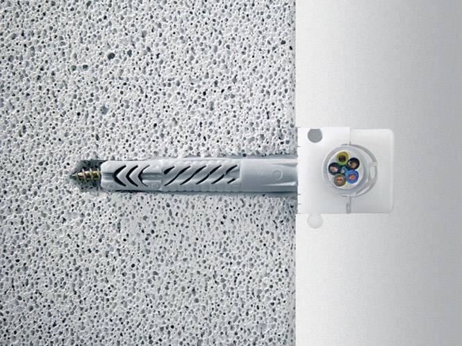 Une vis avec un chevillet est fixée dans un mur en béton. À droite se trouve un récipient en plastique qui montre plusieurs câbles colorés.