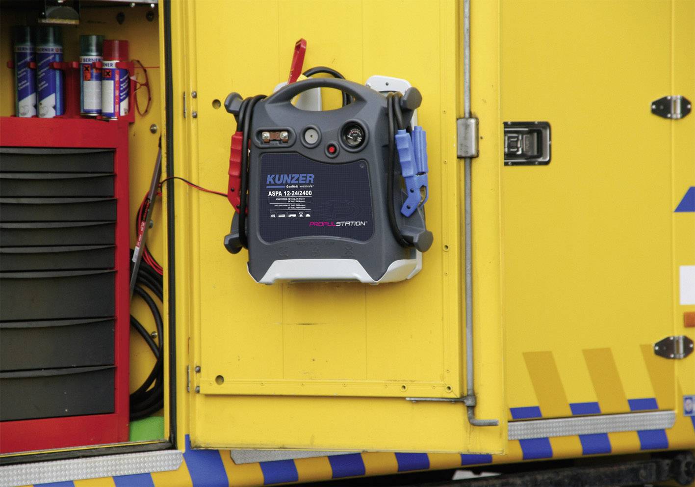 Un véhicule jaune avec un dispositif de démarrage portable à l'extérieur, entouré de divers appareils et câbles.