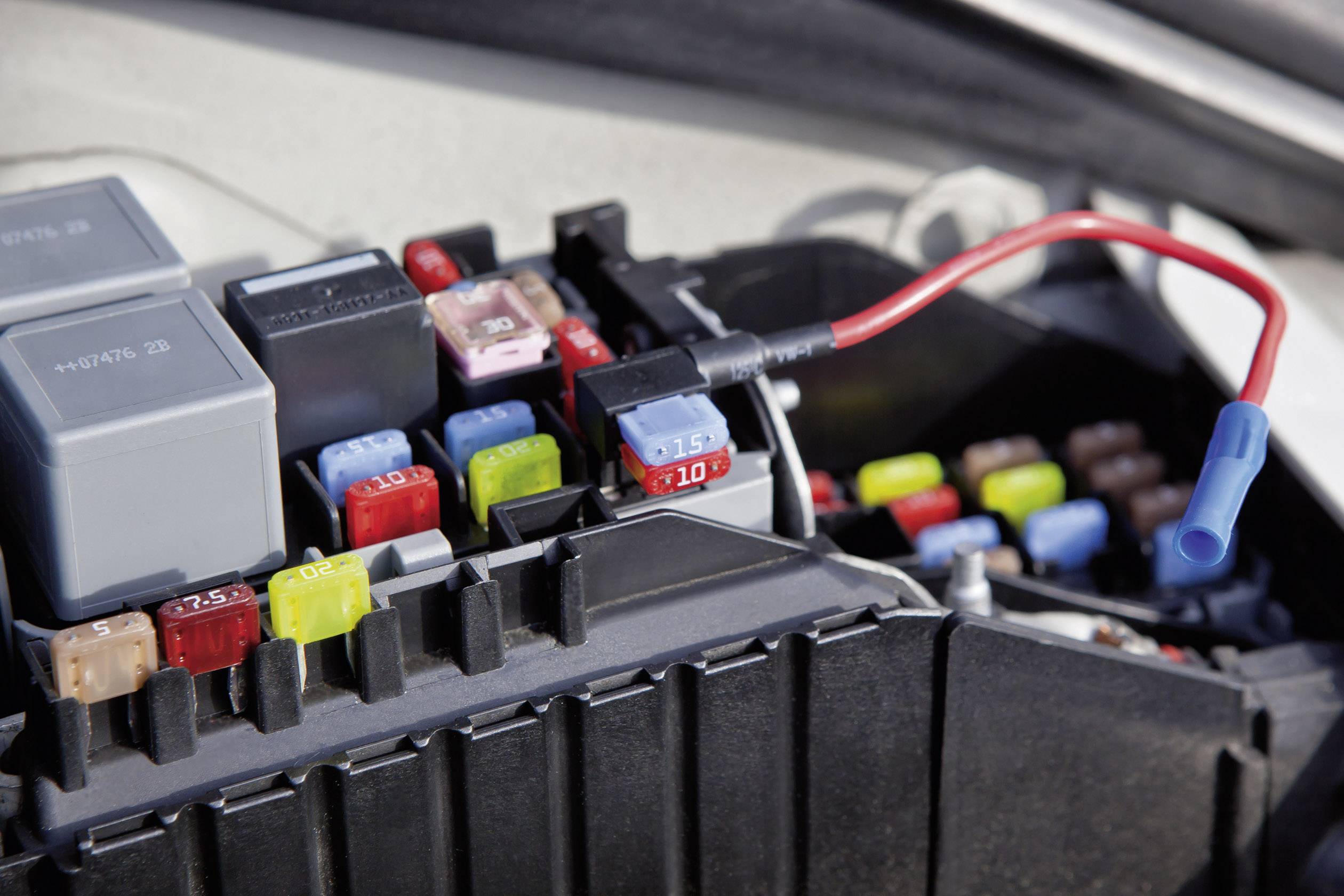 Boîte à fusibles automobile avec différents fusibles colorés et un multimètre testant le flux électrique.