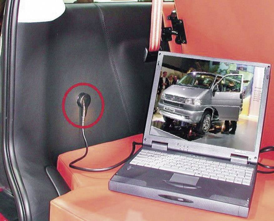 Un ordinateur portable affiche l'image d'une voiture sur un écran dans un intérieur de véhicule. Un câble noir est connecté à l'ordinateur portable.