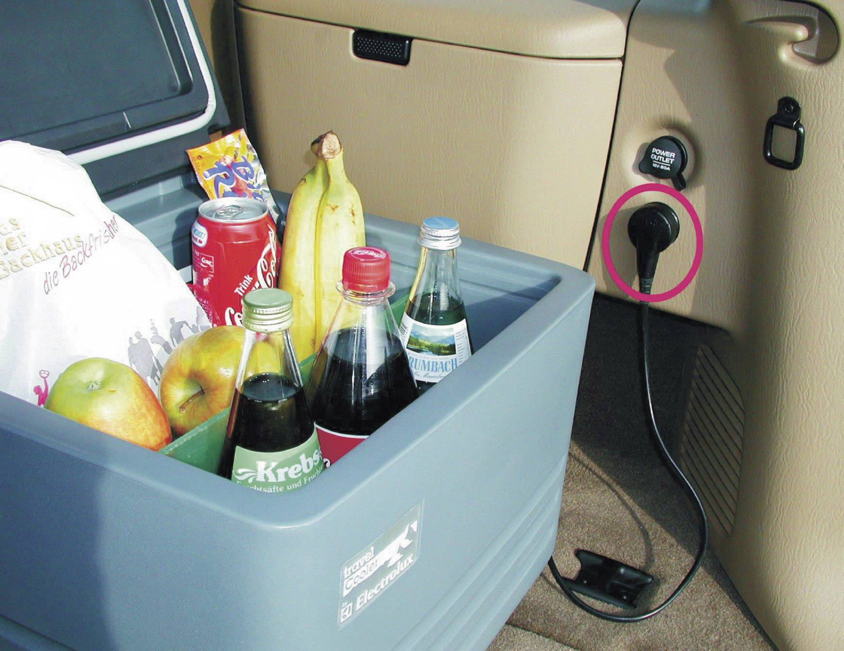 'Glacière dans la voiture avec le couvercle ouvert, remplie de boissons, de fruits et de collations. Branchée à la prise 12V du véhicule.'