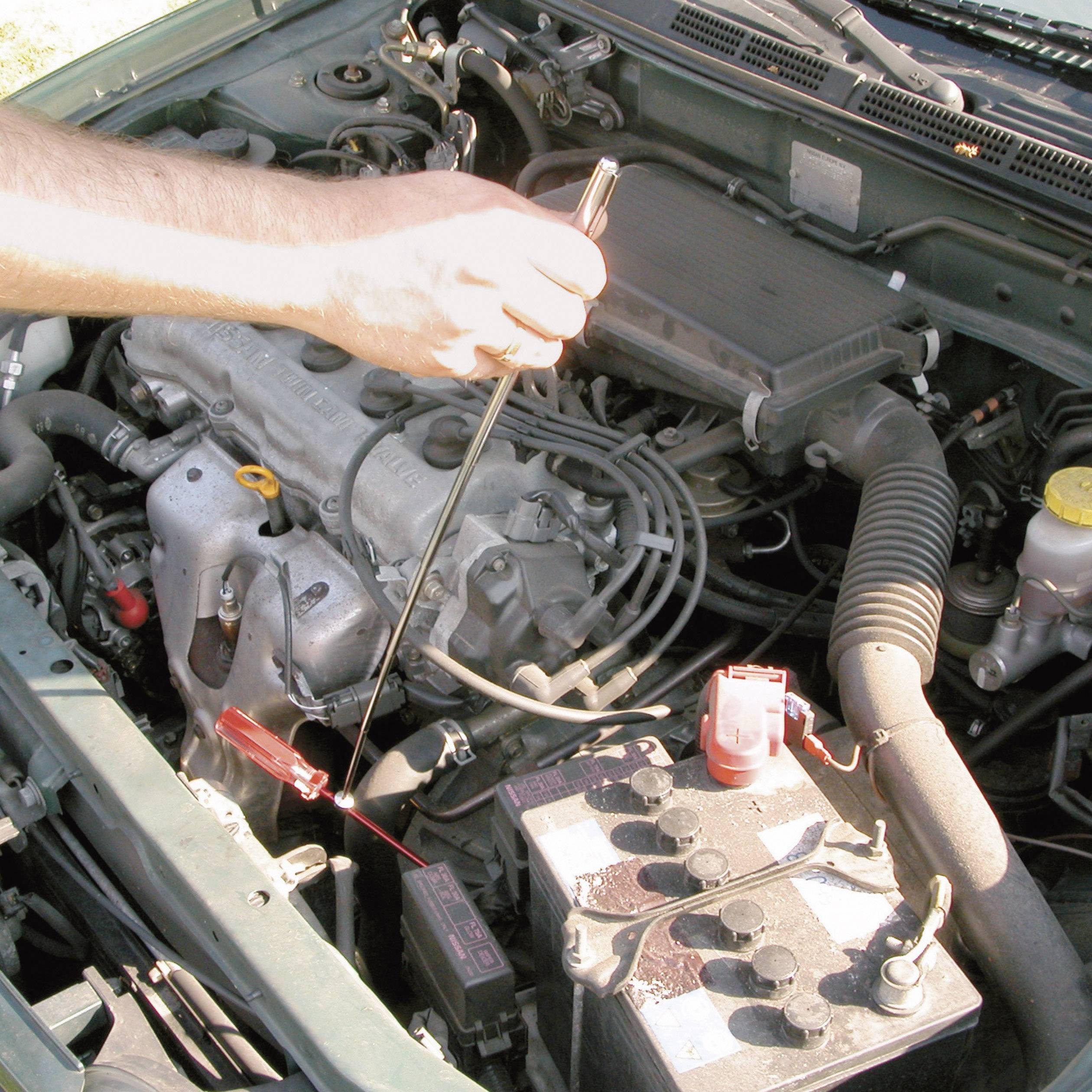 Une personne vérifie le niveau d'huile d'une voiture en sortant la jauge de niveau d'huile du moteur. Le capot est ouvert.