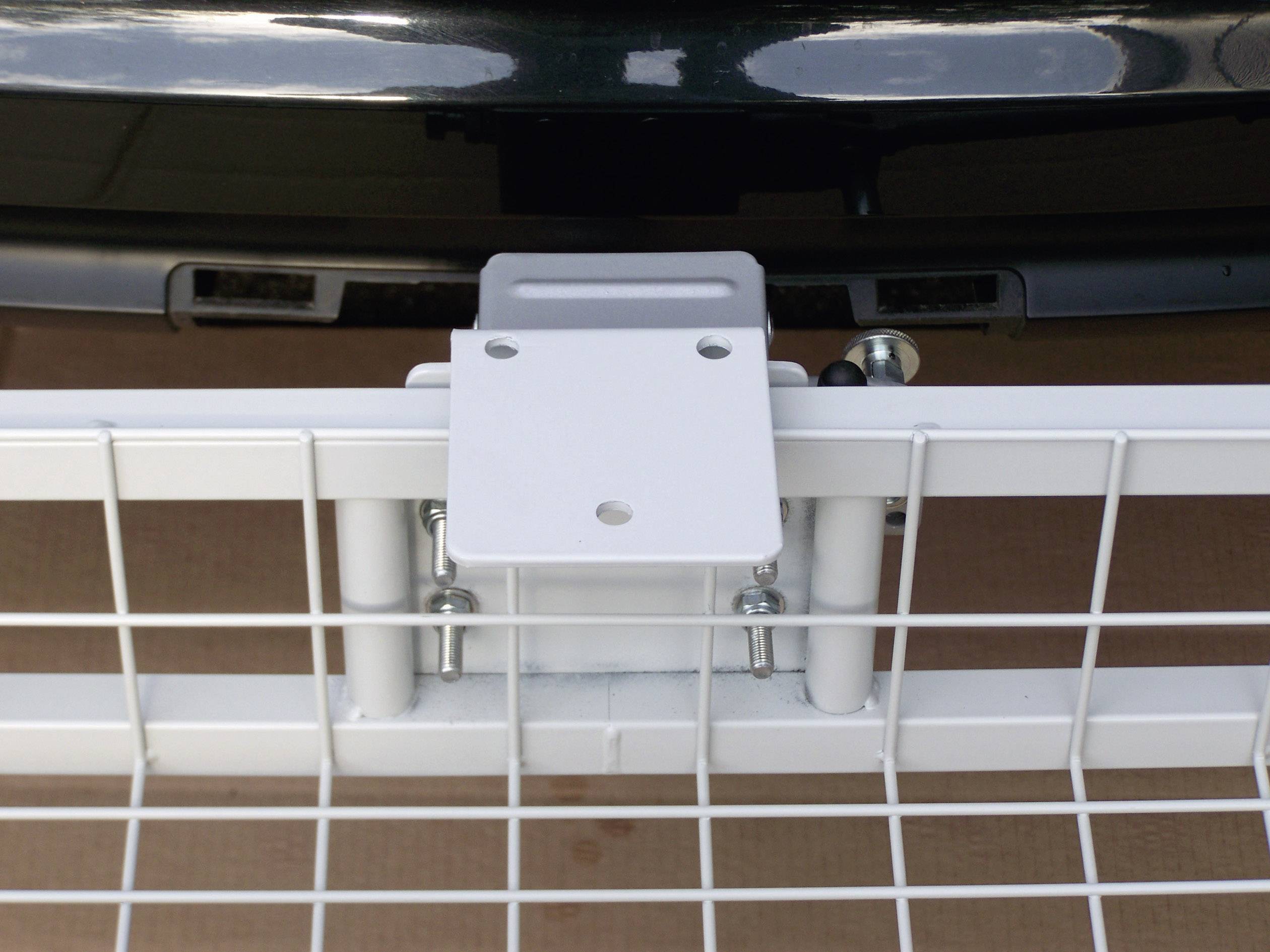 Un support métallique blanc est fixé à l'arrière d'une voiture. Le support est de type grille et attaché avec des vis.
