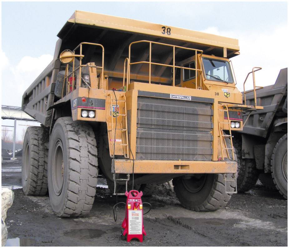 Un grand camion-benne jaune est stationné sur un chantier de construction. Au premier plan, on peut voir un extincteur rouge.