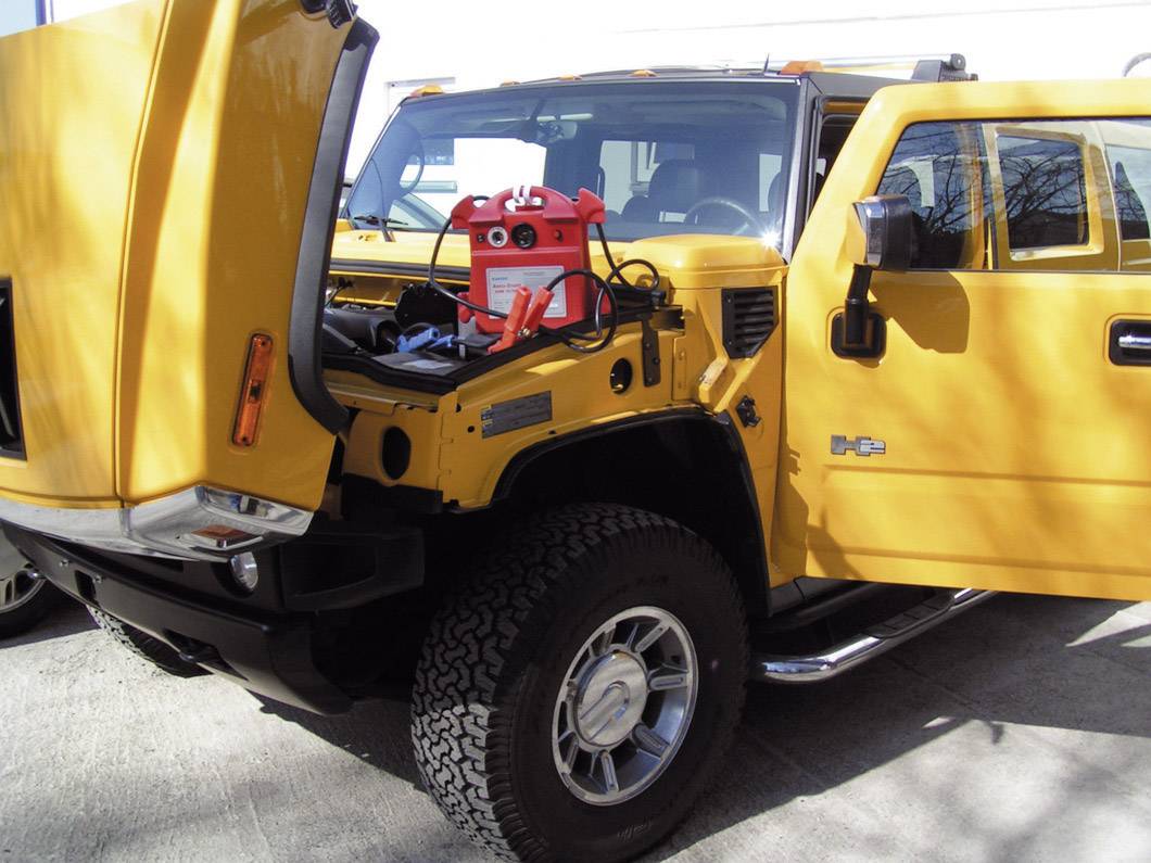 SUV jaune avec le capot ouvert, un chargeur est branché dans le compartiment moteur. Le véhicule est stationné sur une surface en béton.