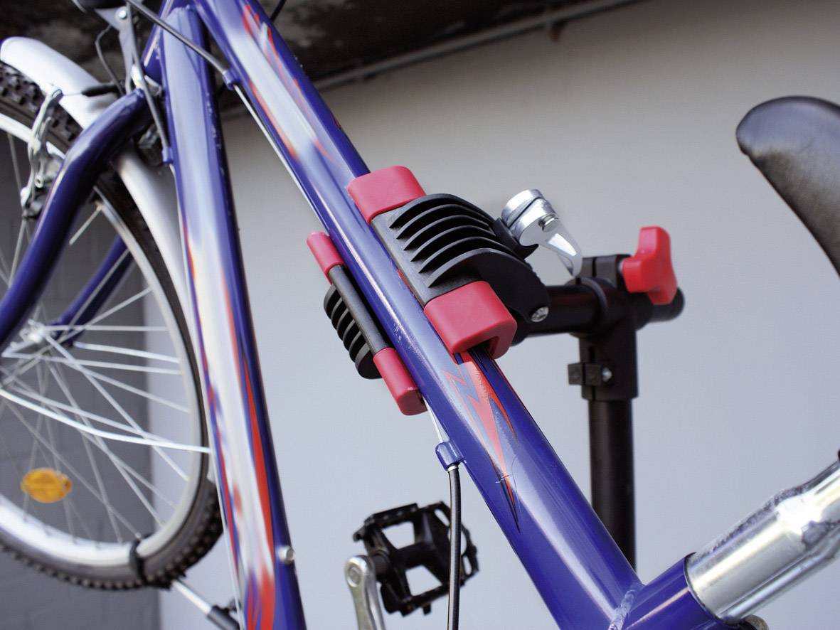 Un vélo est fixé dans un support de montage. Le cadre est bleu avec des filets décoratifs rouges. La roue avant est partiellement visible.