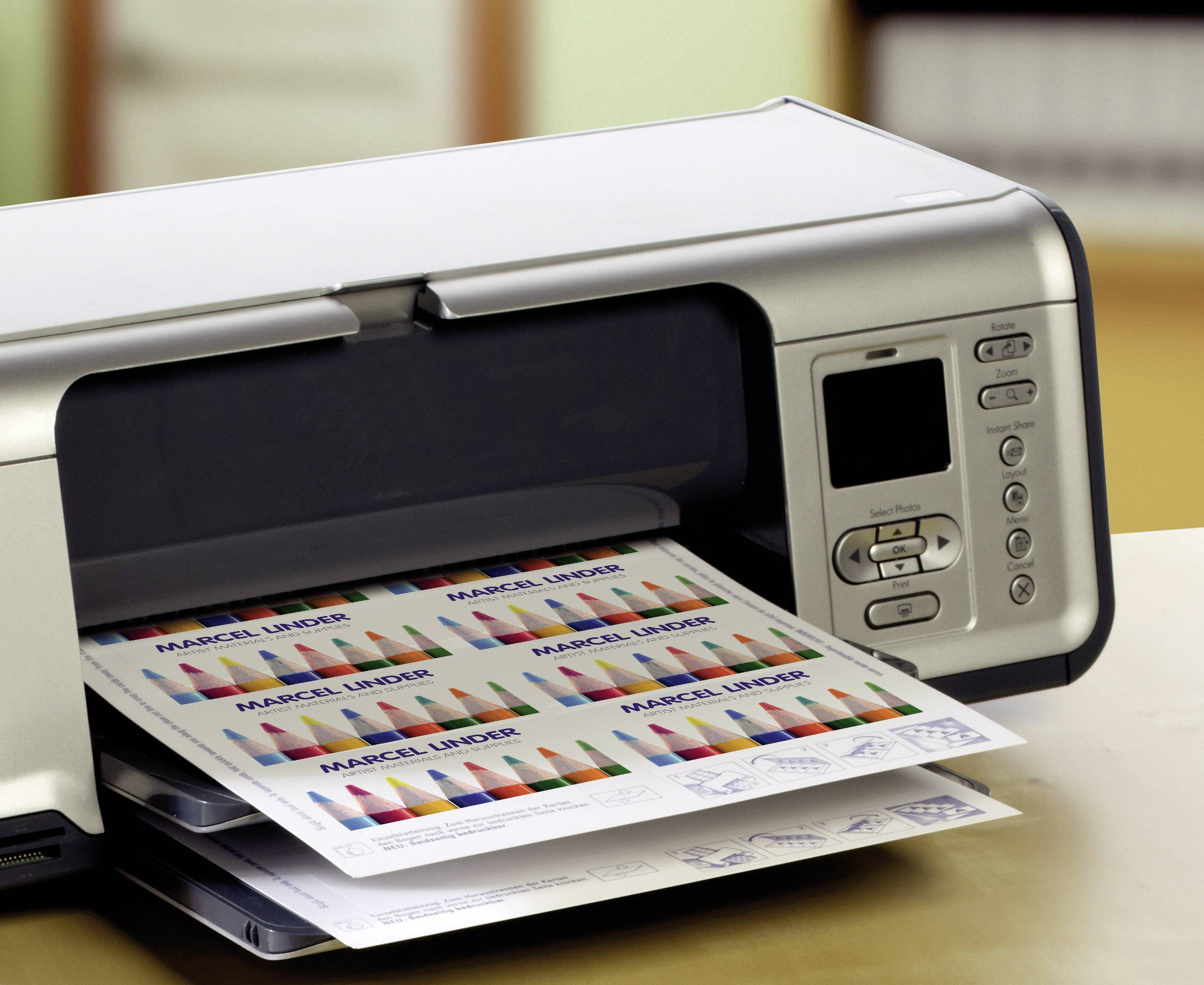 Un imprimante sur une table imprime des feuilles en couleur avec des graphiques et le texte 'MUSTER INNER'. Le panneau de commande avec des touches est visible.