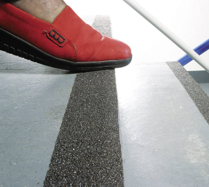 Une personne portant une chaussure rouge monte une marche équipée d'une bande antidérapante.