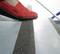 Une personne portant une chaussure rouge monte une marche équipée d'une bande antidérapante.