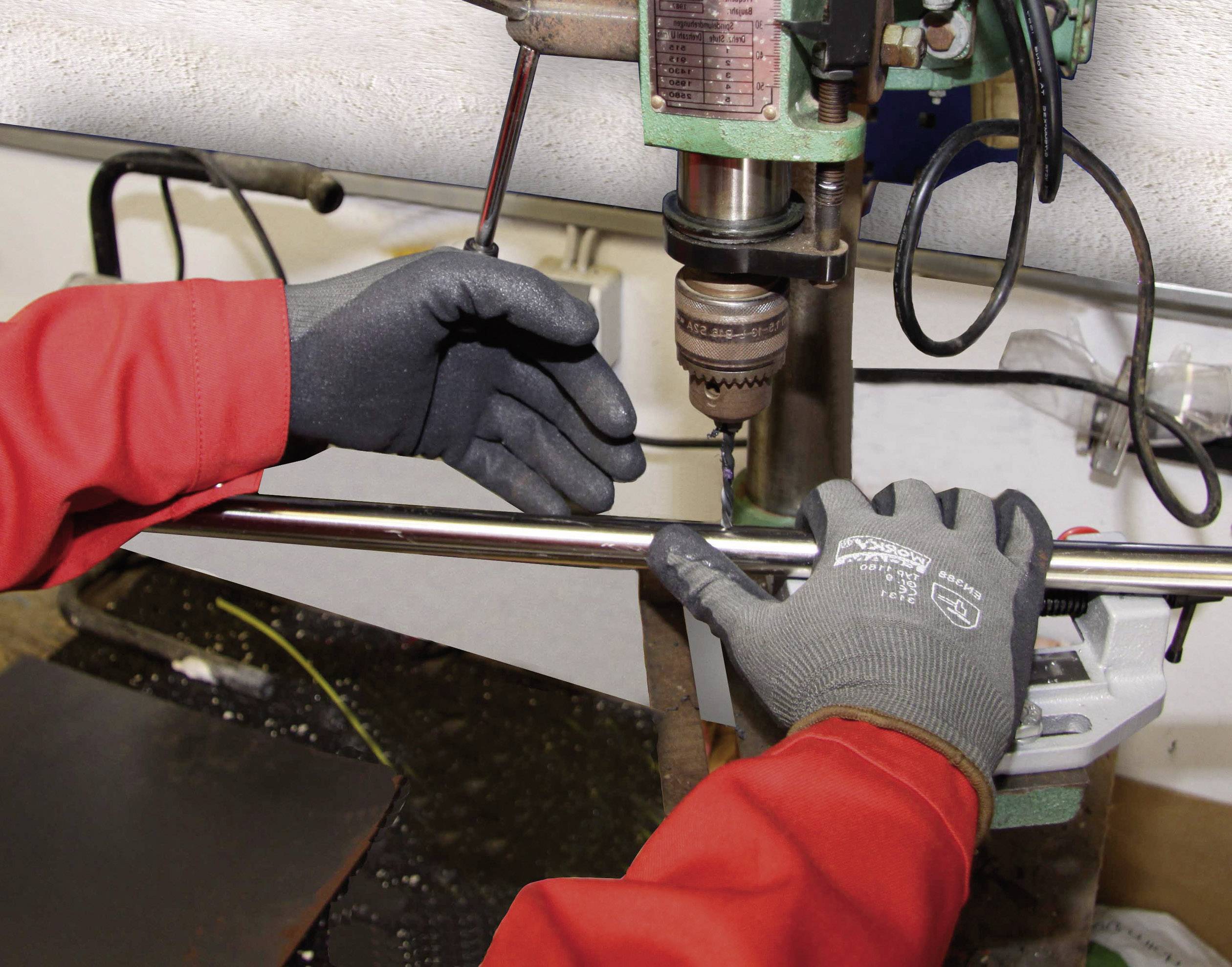 Une personne portant des gants de travail rouges utilise une perceuse à colonne dans un atelier. L'accent est mis sur la sécurité et la précision.