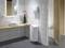 Salle de bain moderne avec lavabo, miroir, distributeur de serviettes et un vase avec une fleur rose sur une étagère en bois. Porte des toilettes partiellement ouverte.