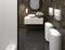 Une salle de bain élégante avec des carrelages sombres et un miroir rond. Un lavabo blanc avec un arrangement floral est posé sur un meuble suspendu.