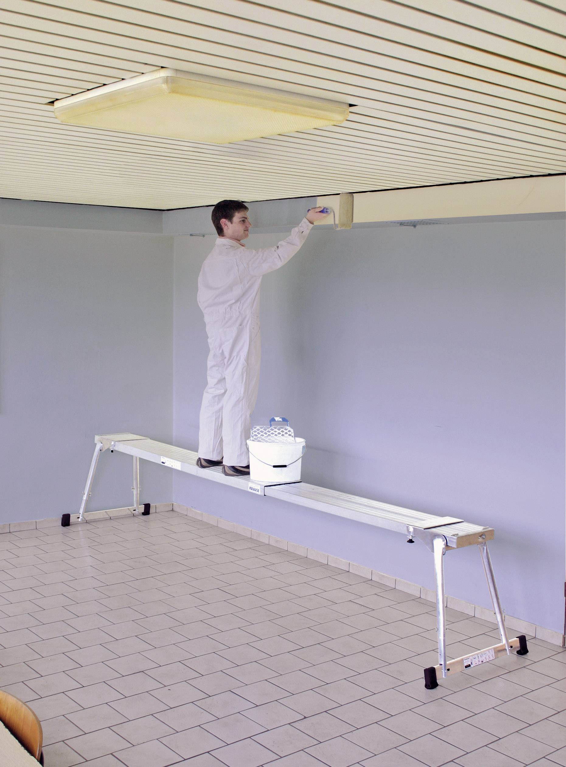 Une personne peint le plafond, debout sur une longue échelle dans une pièce vide. Un seau de peinture est posé à côté d'elle. Un lieu de travail clair et calme.