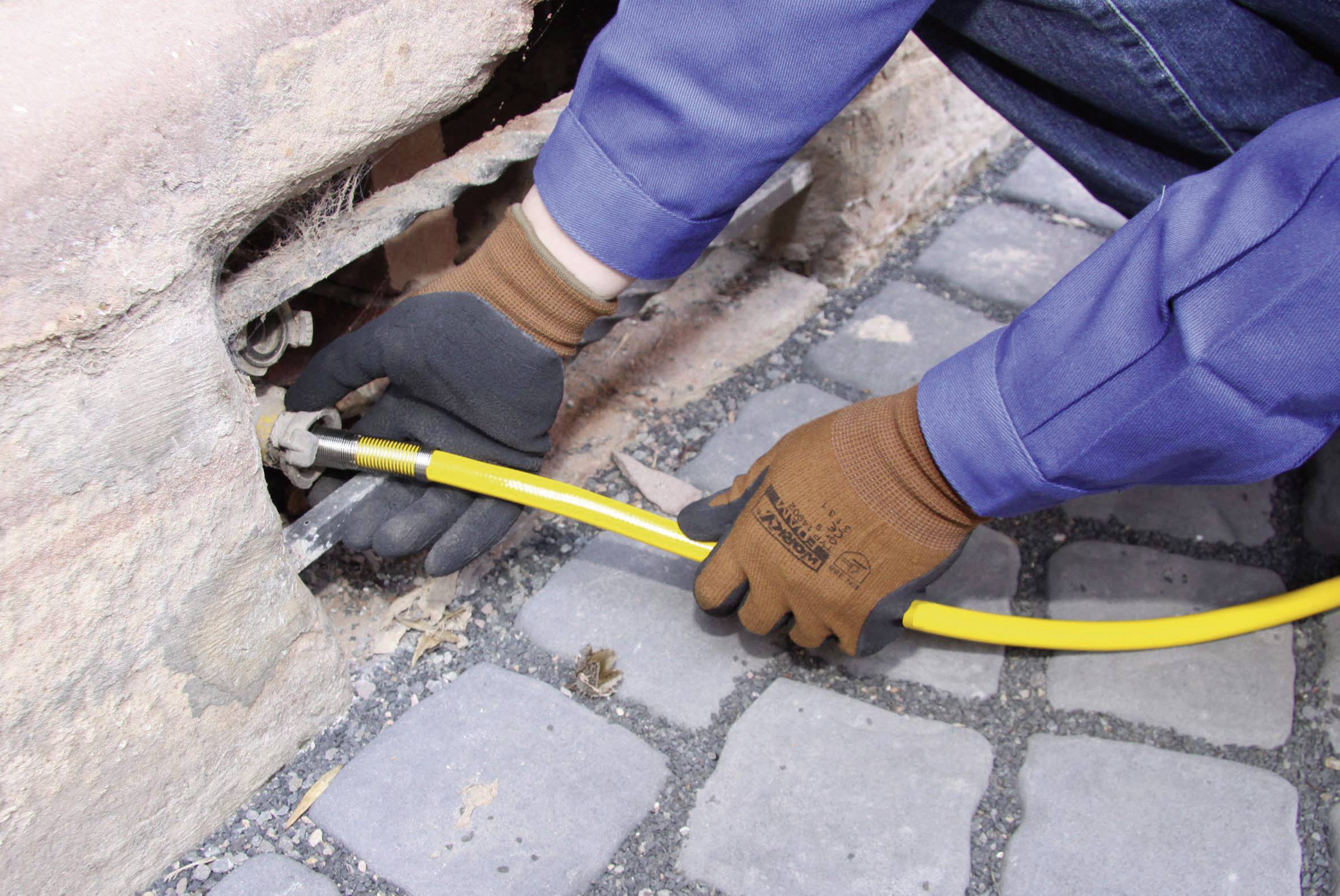 Une personne porte des gants de travail et branche un câble jaune sur une prise murale, probablement dans le cadre de travaux de construction.