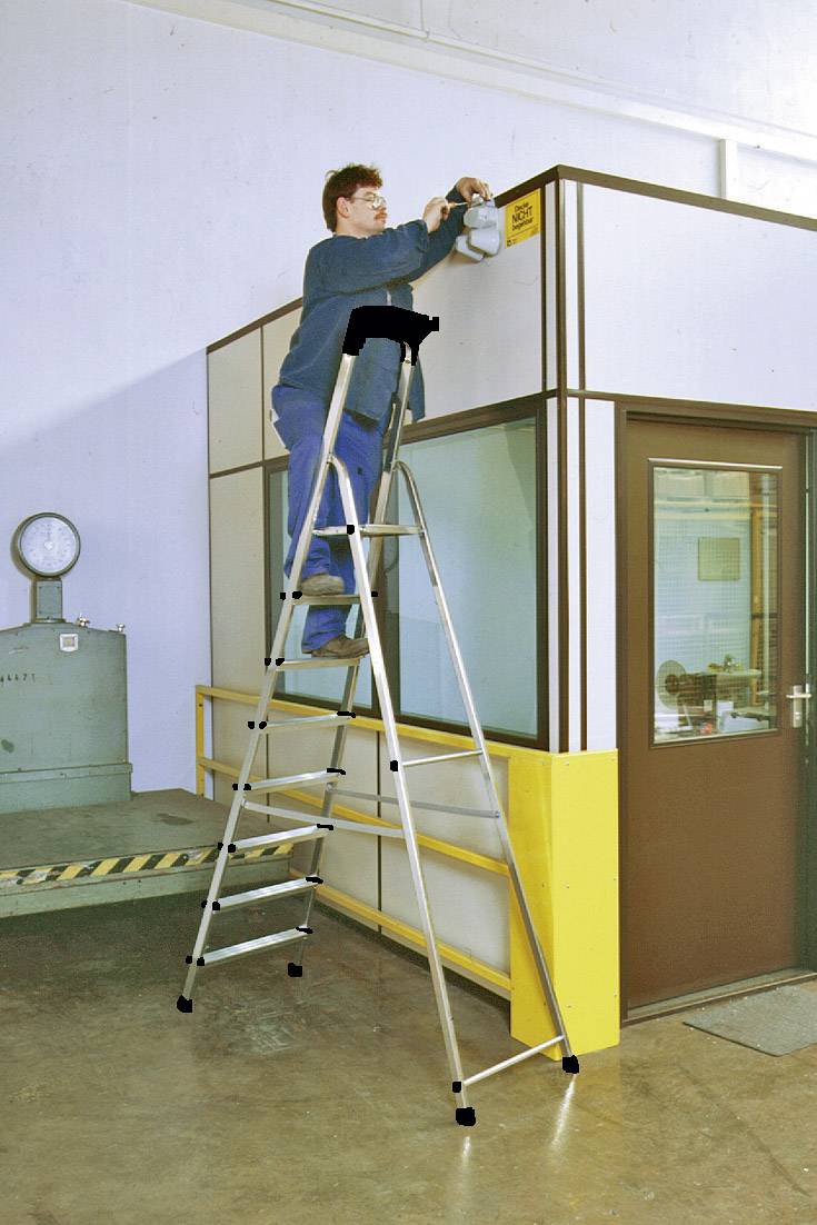 Une personne est debout sur une échelle en aluminium haute et installe ou répare quelque chose en haut d'une cloison dans un espace industriel.