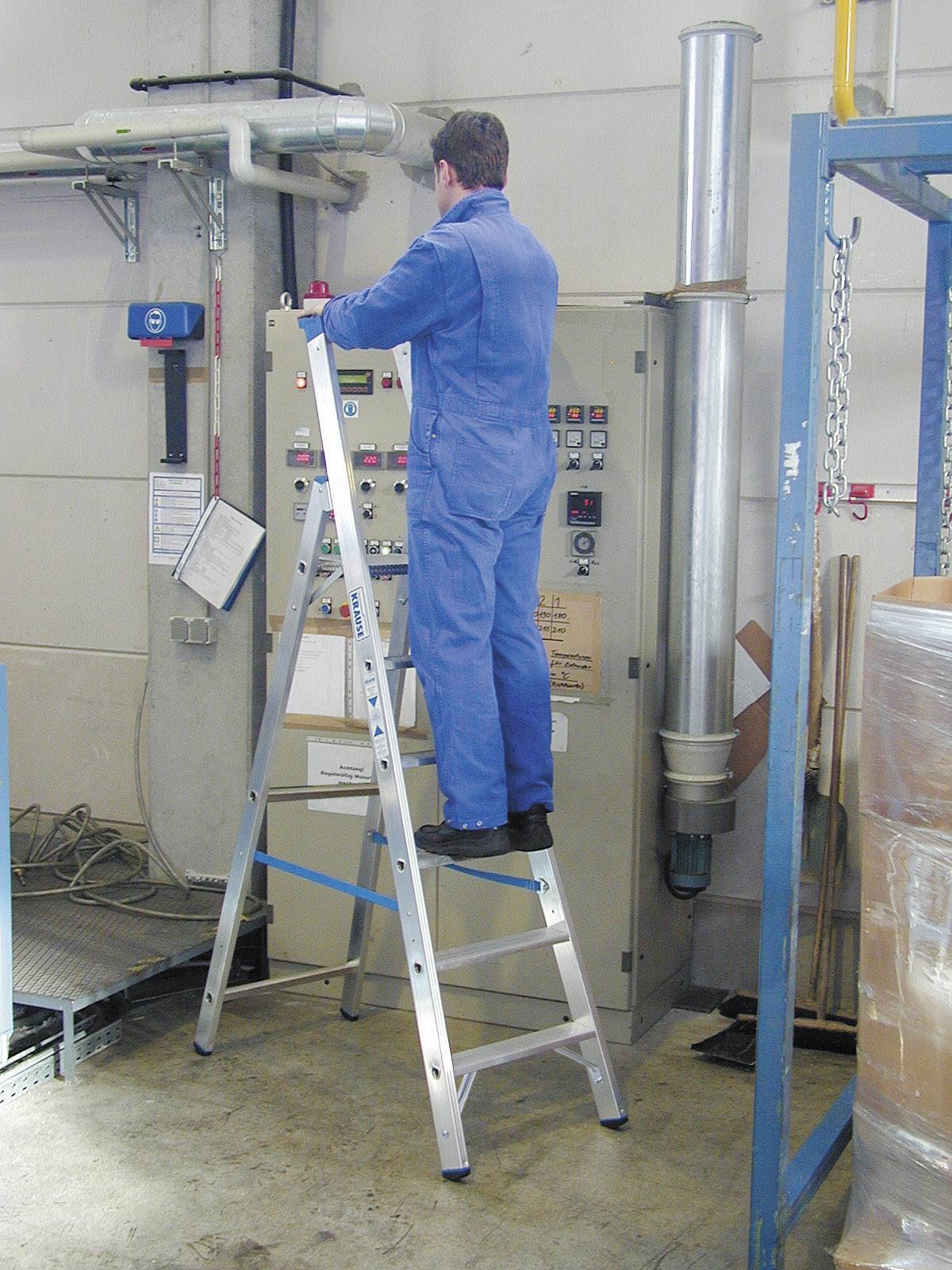 Un homme en tenue de travail bleue est debout sur une échelle pour actionner un interrupteur sur un grand tableau électrique dans un environnement industriel.
