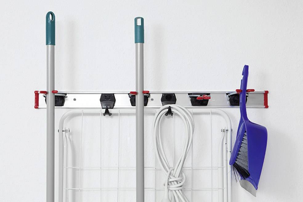 Accessoires de nettoyage sur support mural : deux manches à balai et un balai à main bleu sont suspendus au-dessus d'un étendoir plié.