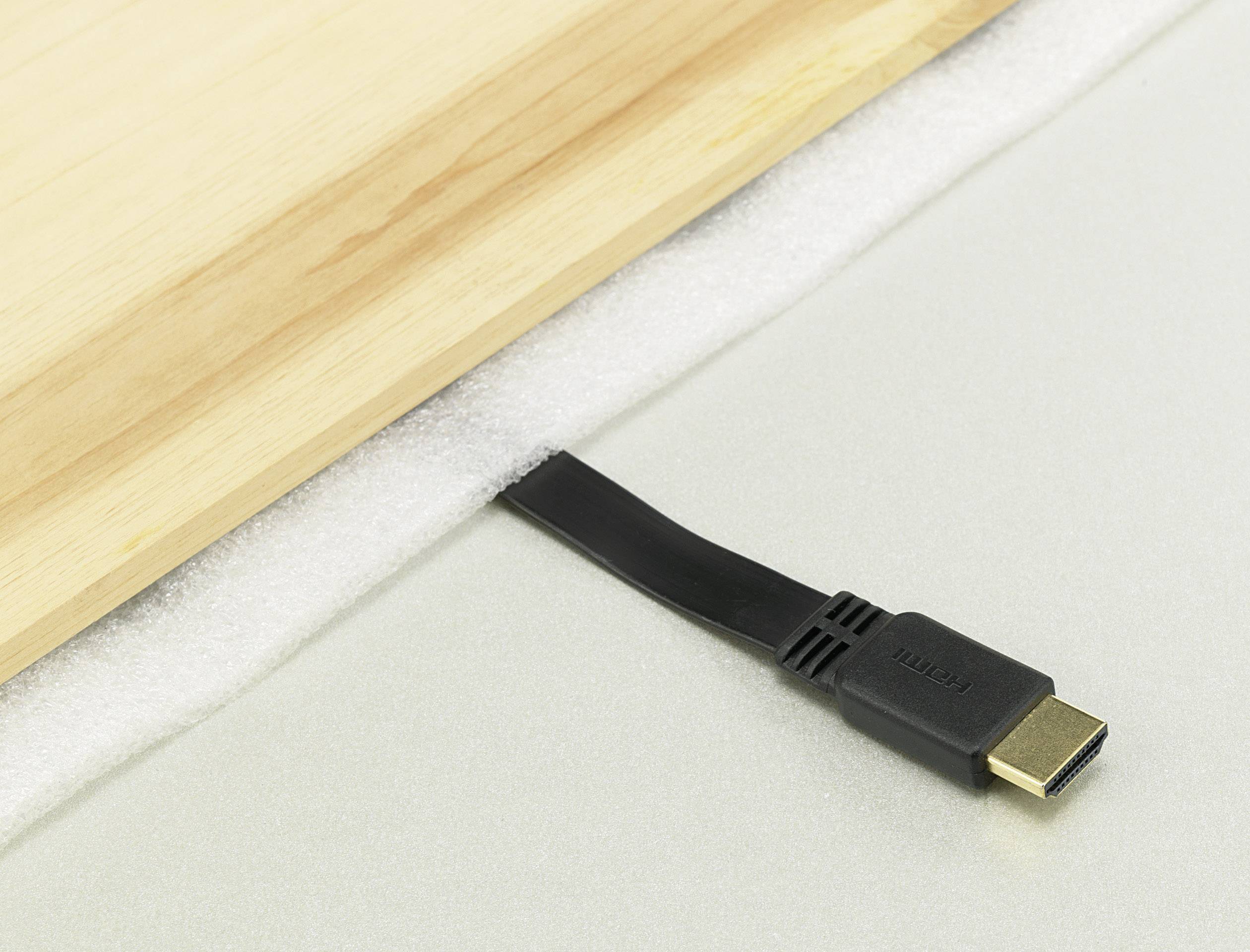 Un câble HDMI noir est posé sur une surface claire texturée, à côté d'une planche en bois.