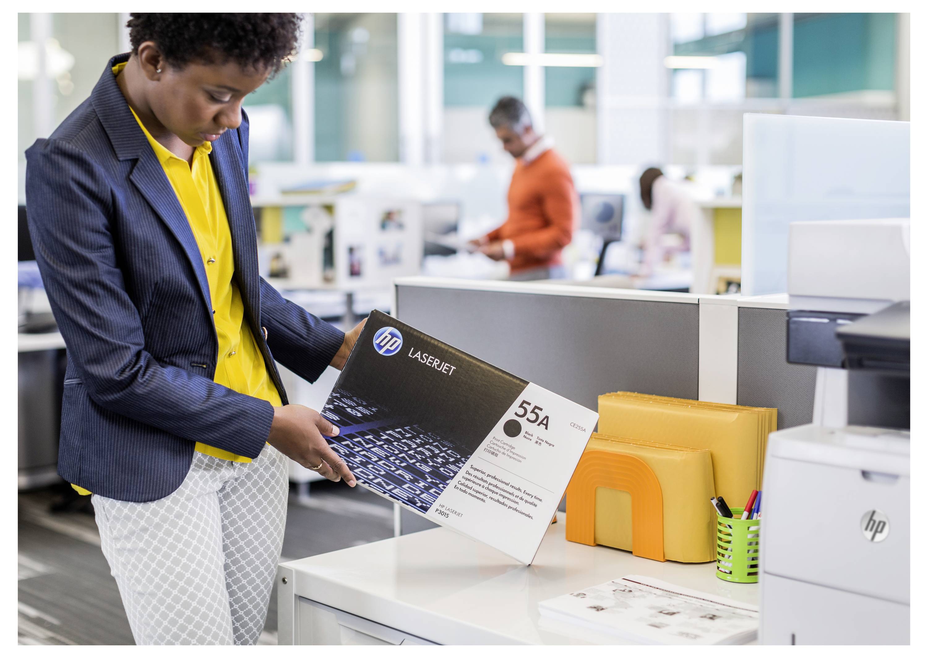 Žena u uredskom prostoru za ispis pregleda kutiju tonera HP LaserJet 55A pored pisača i uredskog pribora.