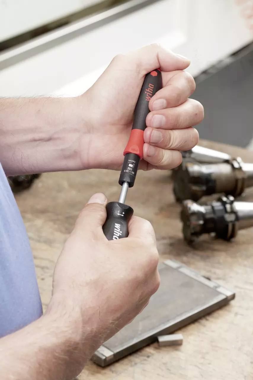 Ruke koje koriste odvijač s izmjenjivim nastavkom na radnoj klupi, s metalnim alatima u pozadini.