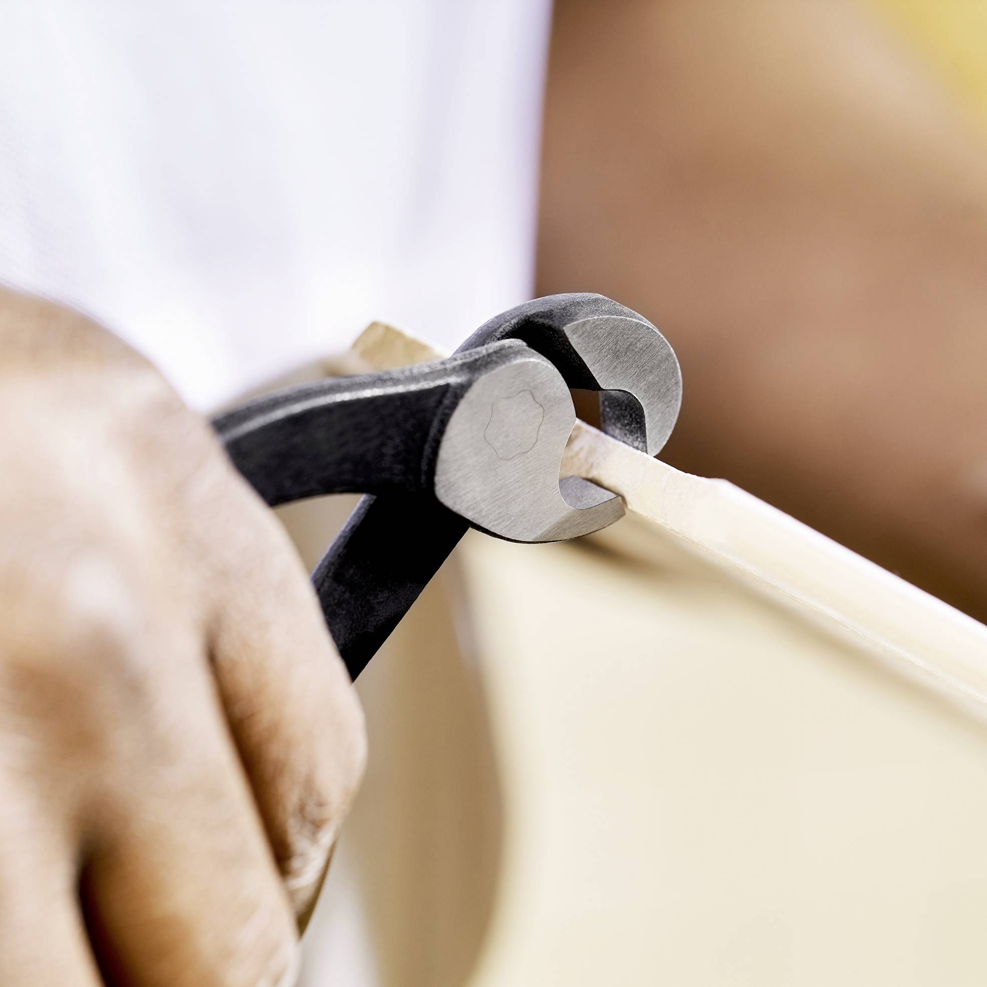 Osoba reže tanki komad drva kliještima. Fokus je na rukama i alatu, vidljivi su detalji komada drva.