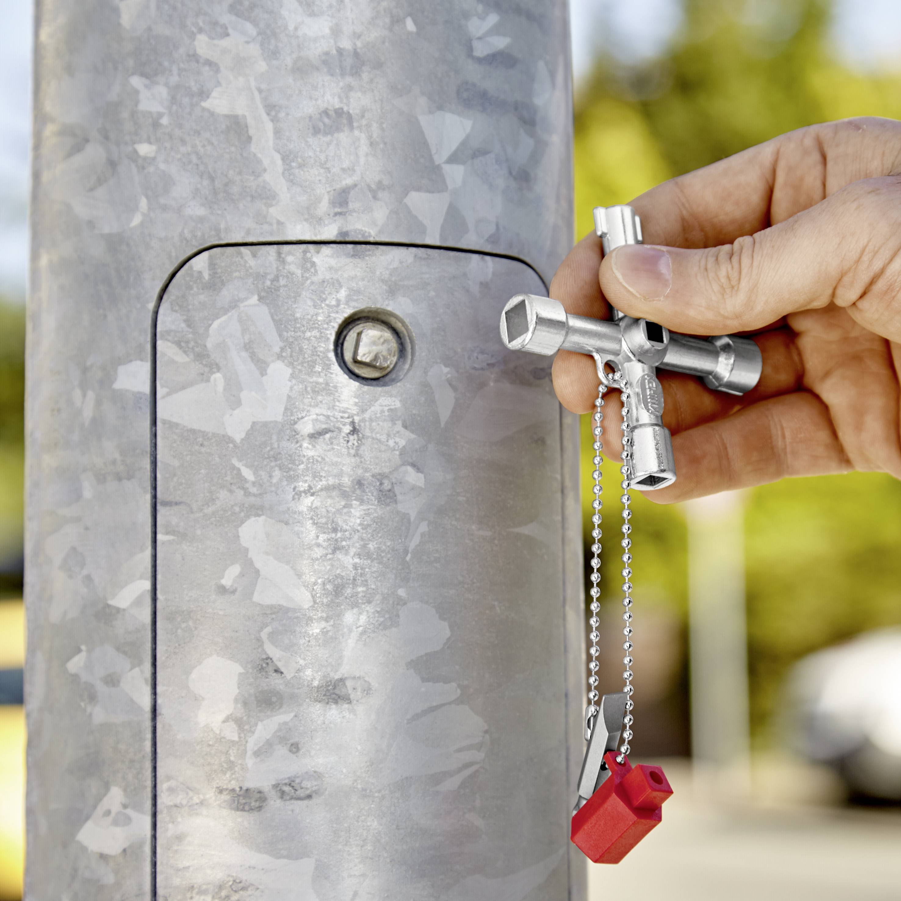 Jedna ruka drži ključni prekidač s nekoliko utora ispred srebrnog ormarića za struju. U pozadini se nejasno nazire zelena boja.