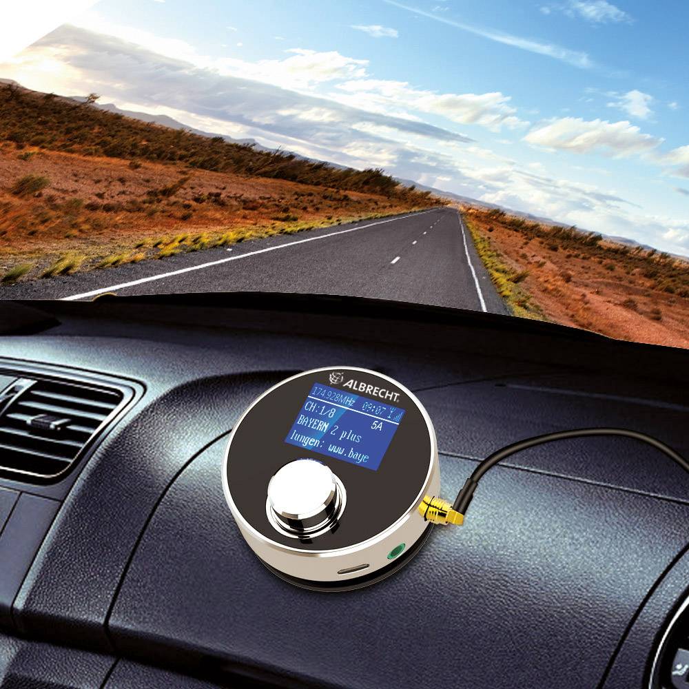 Na instrumentnoj ploči automobila koji vozi kroz countryside, nalazi se radio uređaj. Nebo je plavo s nekoliko oblaka.