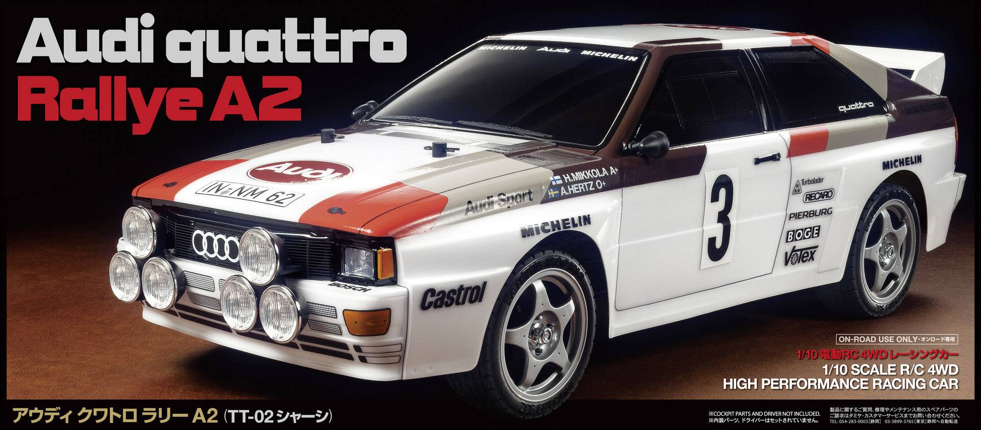 Model automobila Audi Quattro Rallye A2 u mjerilu 1:10, ukrašen rally naljepnicama i far reflektorima, prikazan na nekoj površini.