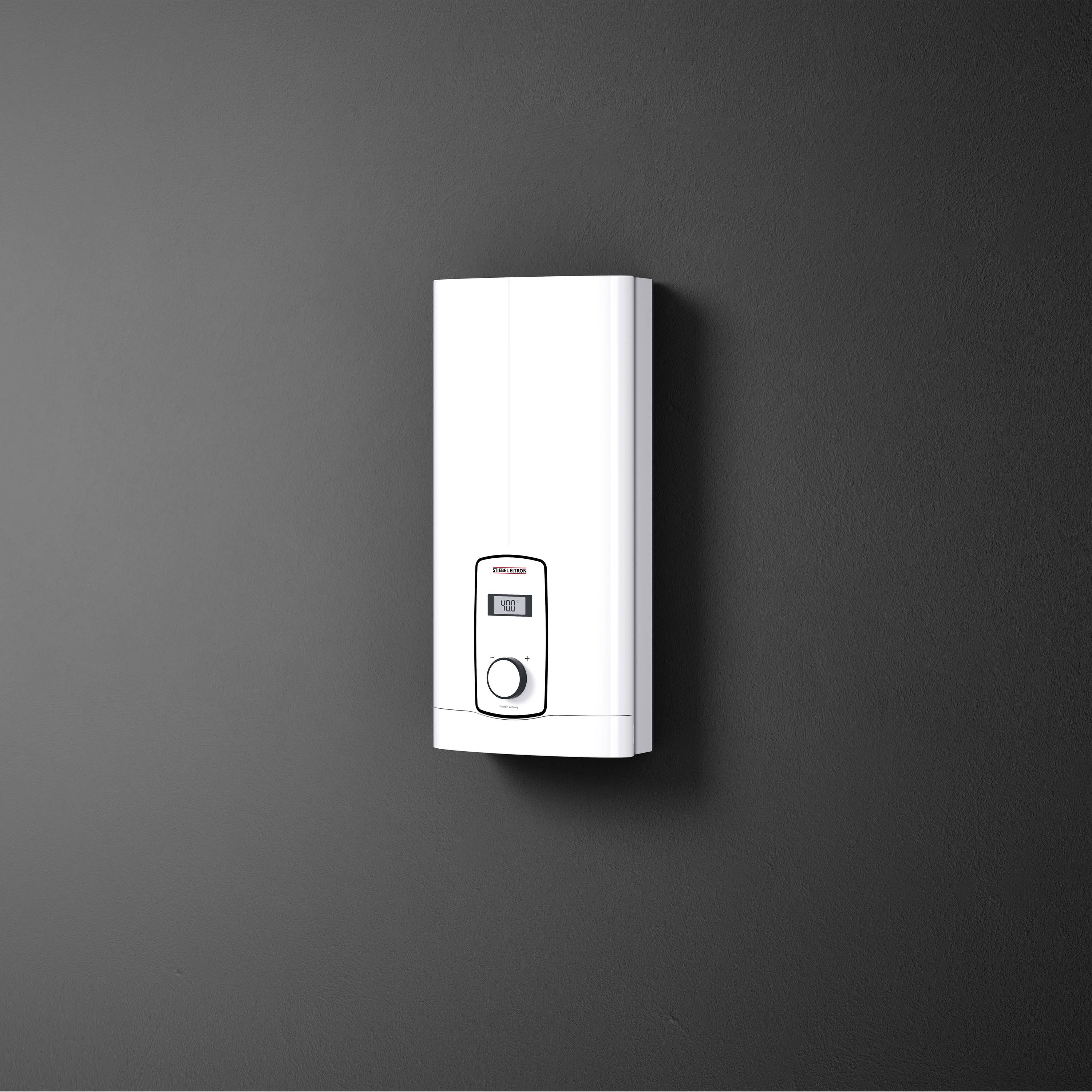 Bijeli električni protočni grijač vode postavljen na crnom zidu, s digitalnim zaslonom i tipkama za regulaciju temperature.