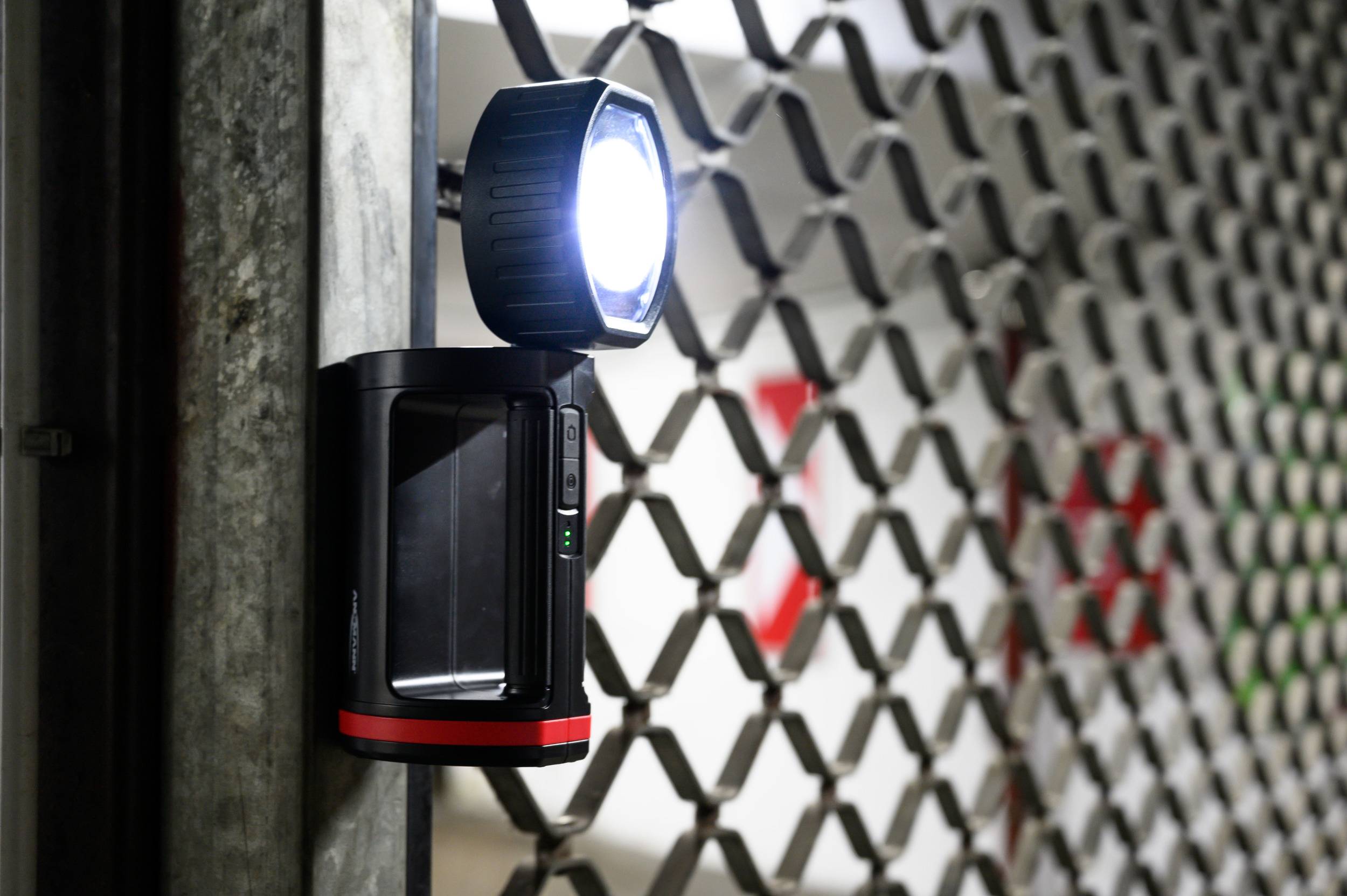 Sigurnosna kamera sa jakim svjetlom pričvršćena je za metalnu ogradu. U pozadini se djelomično nazire crveni znak.