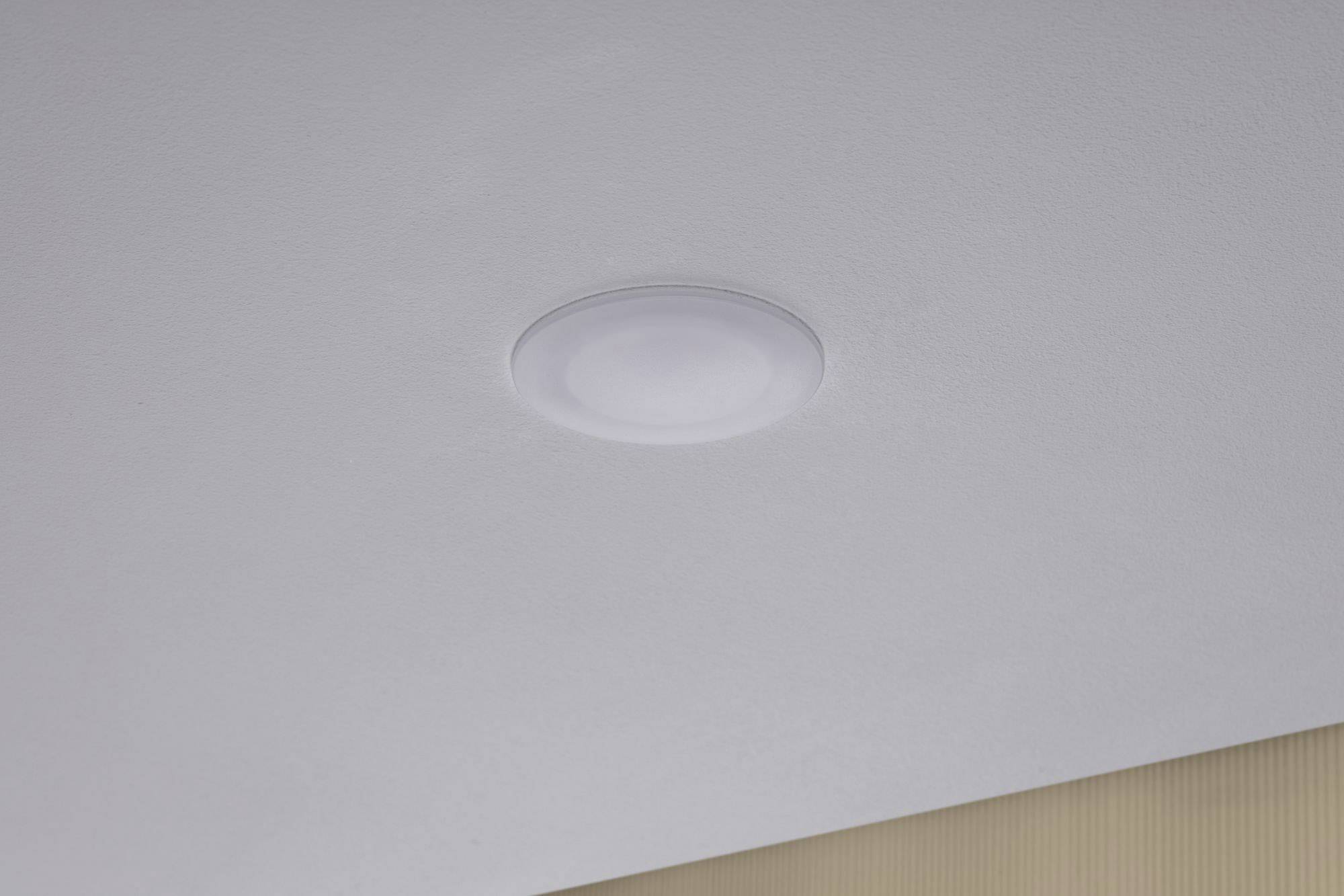 Bijela, okrugla stropna lampa pričvršćena je na svijetlosivom stropu.