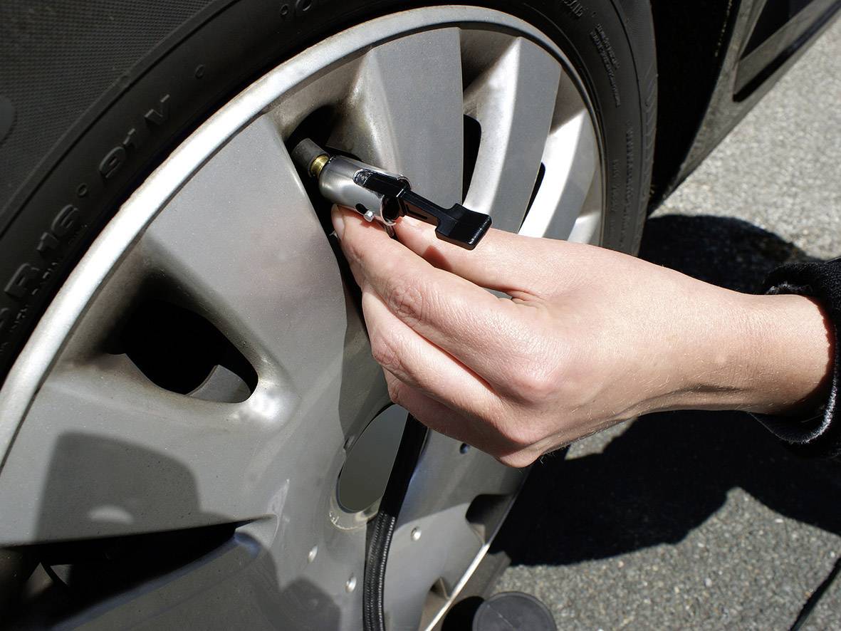 Ruka provjerava tlak u pneumatiku automobila pomoću mjerača tlaka.
