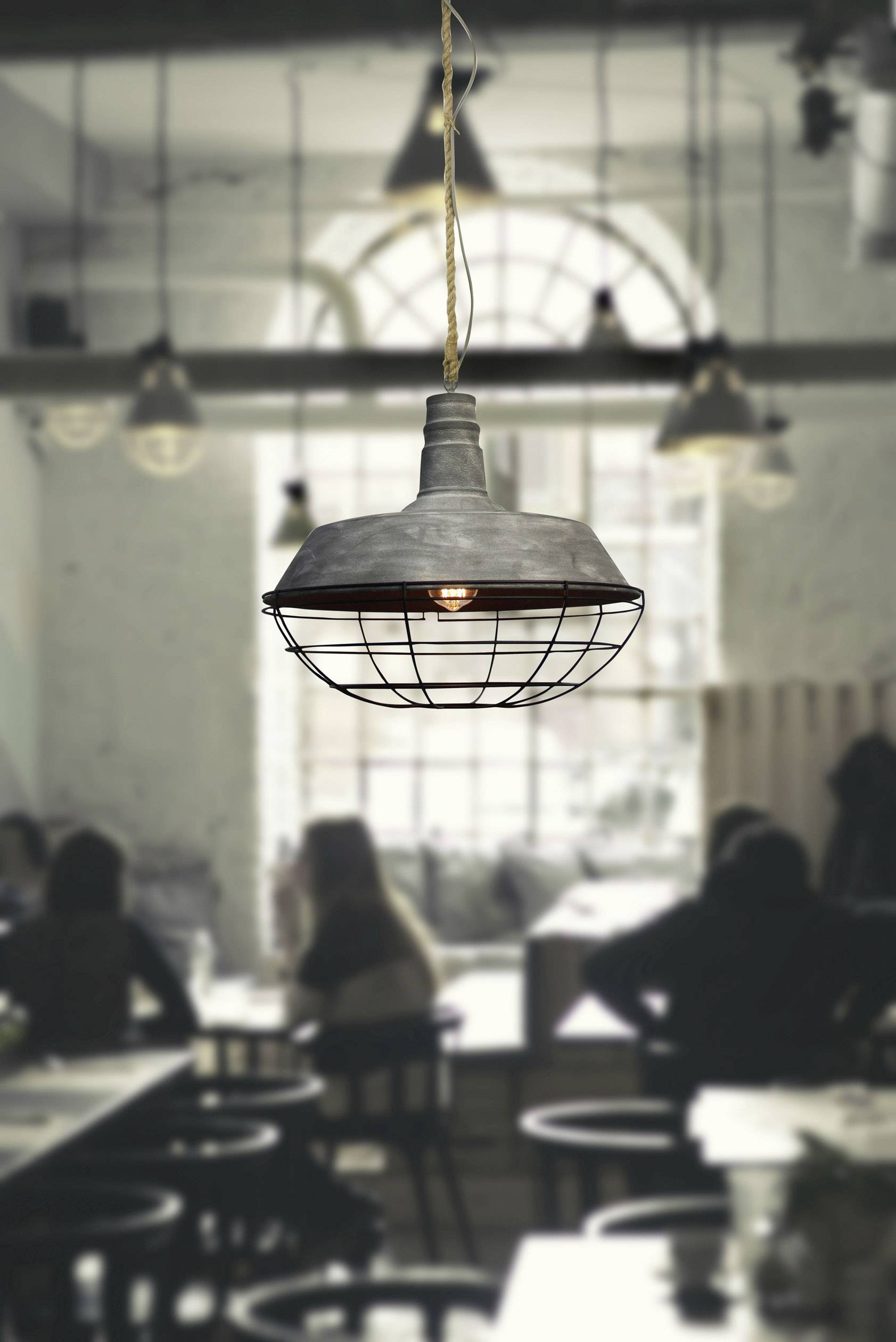 Viseća metalna lampa osvjetljava prostoriju nejasnim siluetama ljudi u kafiću ili restoranu, stvarajući ugodnu atmosferu.